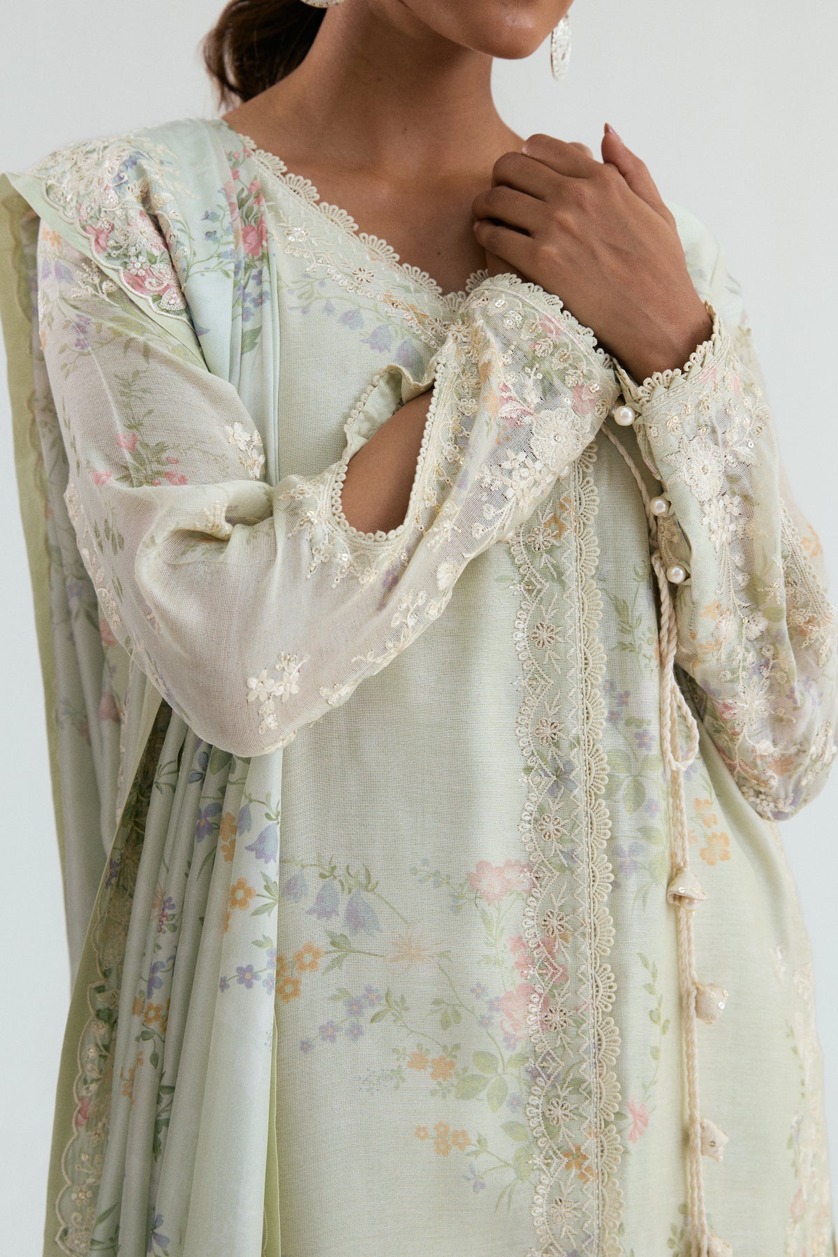 Close-up of pearl button sleeve detail and handcrafted tassels on a pastel Pakistani designer kameez