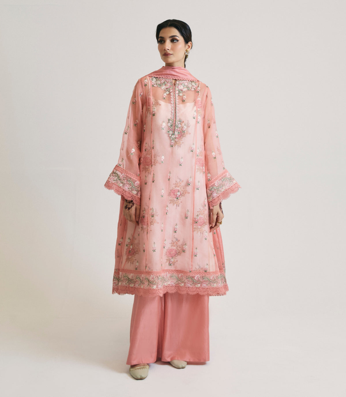 The Pink Kalidaar Set by Mannam is a blush-pink kataan organza peshwas — a flared A-line silhouette with lace-trimmed neckline and sleeve cuffs, designed for Pakistani weddings and Eid celebrations