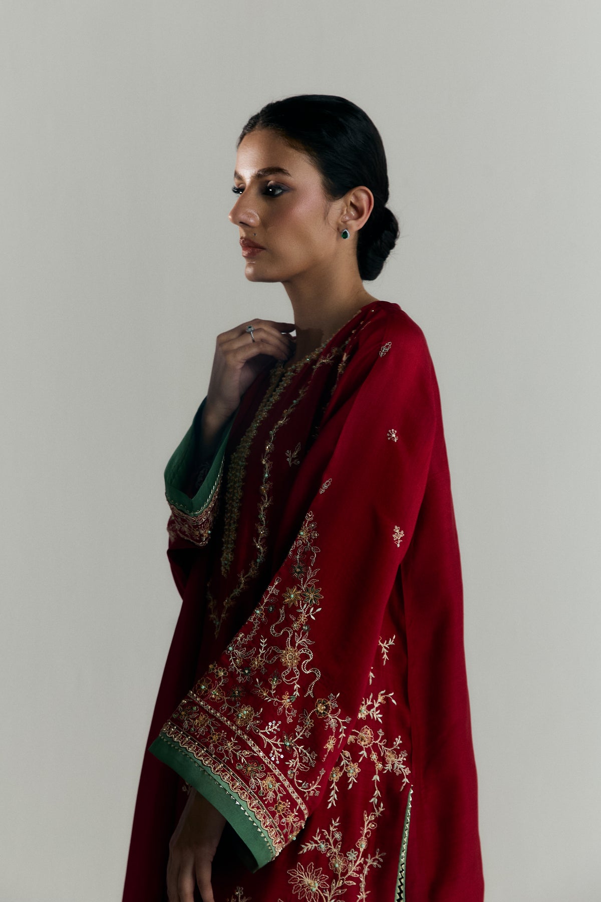 Side view of scarlet khaadi silk Pakistani kameez with gota-lined hem and wide-hem embroidered trousers by Mannam