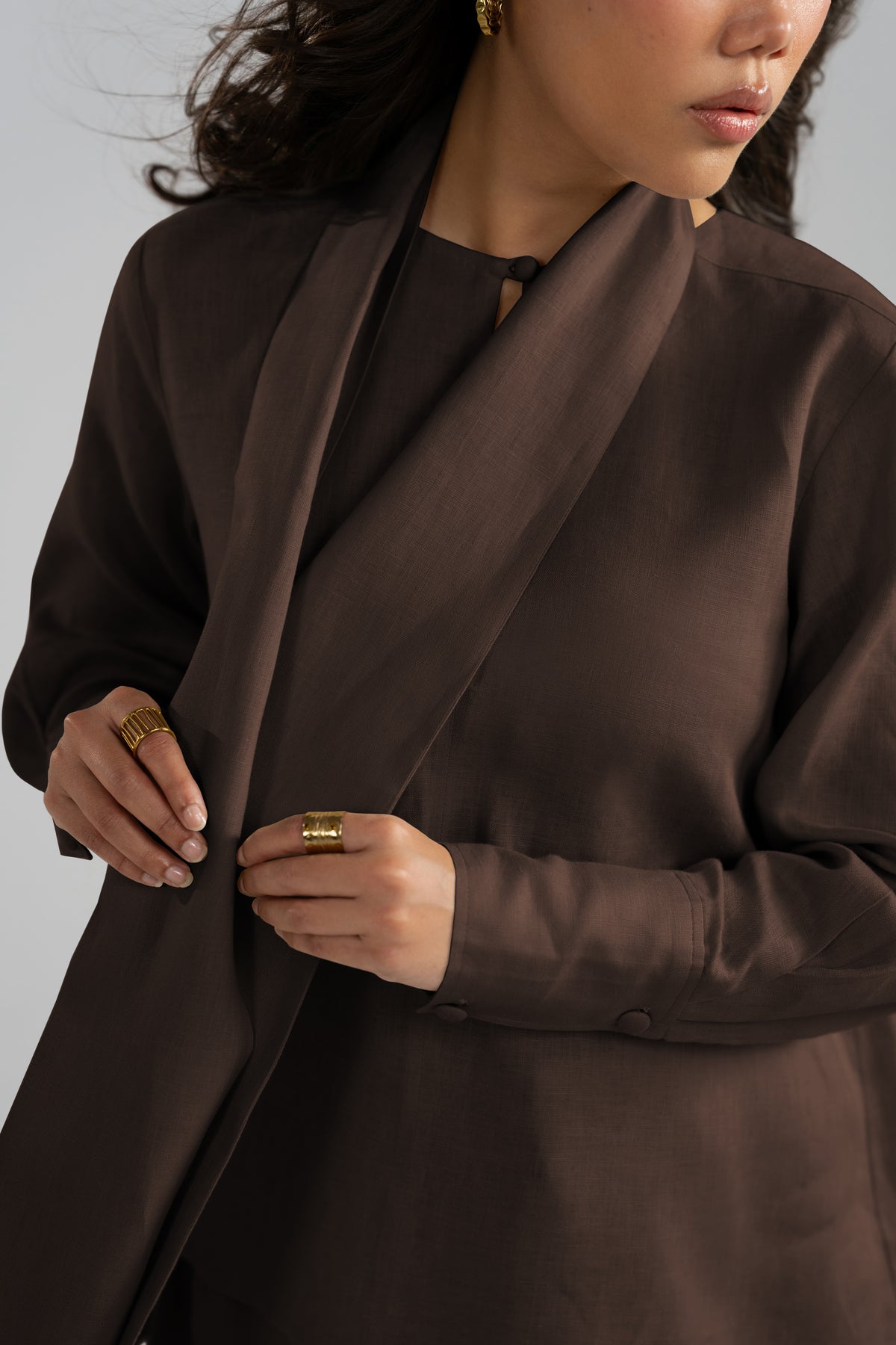 A close-up of a dark brown chestnut wrap-style kameez with a scarf, paired with gold rings and earrings.