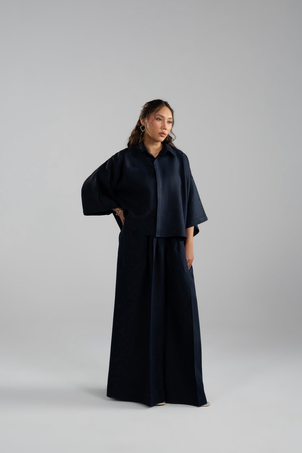 Woman in navy linen co-ord set mid-movement, showing wide-leg trouser drape and sleeve volume