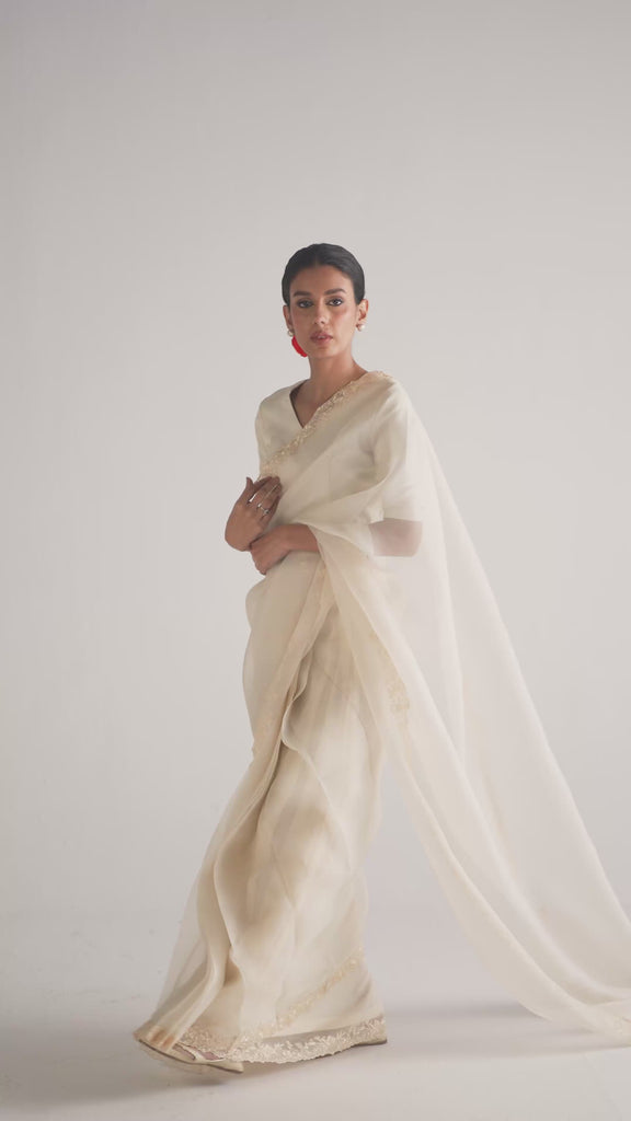 The Chantilly Sari Set by Mannam is a Pakistani ready-to-wear organza sari in chantilly cream, featuring Ghara-style floral embroidery along the border. It comes complete with a pure silk half-sleeve blouse with an adjustable tie-back, the set sari, and a petticoat