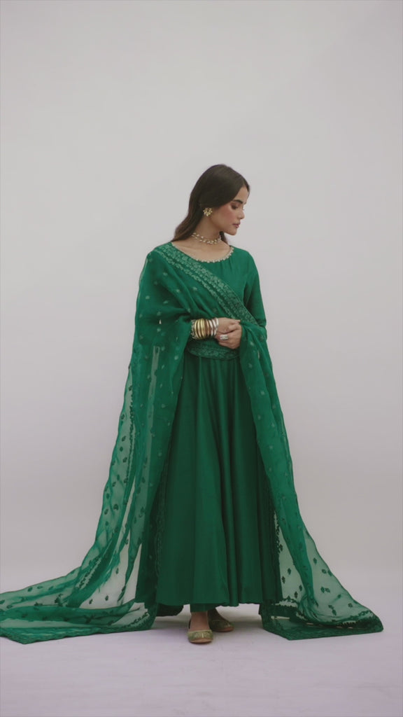 The Emerald Kalidaar Set by Mannam is a pure raw silk peshwas in deep emerald green, featuring hand-embellished detailing at the neckline and sleeve hem. It comes with pure raw silk trousers and a pure organza dupatta with an embroidered floral border.
