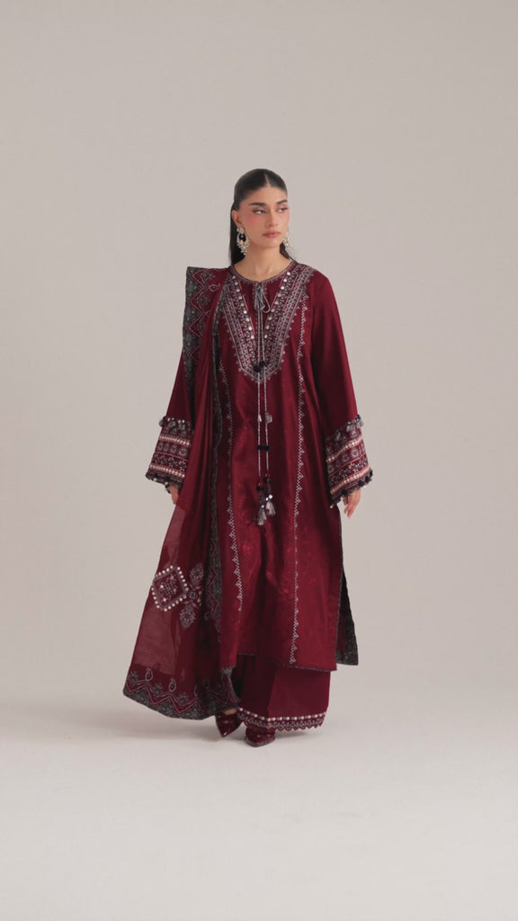 The Saffron Set by Mannam is a deep maroon Pima cotton long kameez featuring Sindhi-inspired embroidery with sequin detailing on the neckline and sleeves, decorative tassels and ajrak accents, paired with wide-leg trousers and an ajrak-print dupatta with scalloped embroidery.