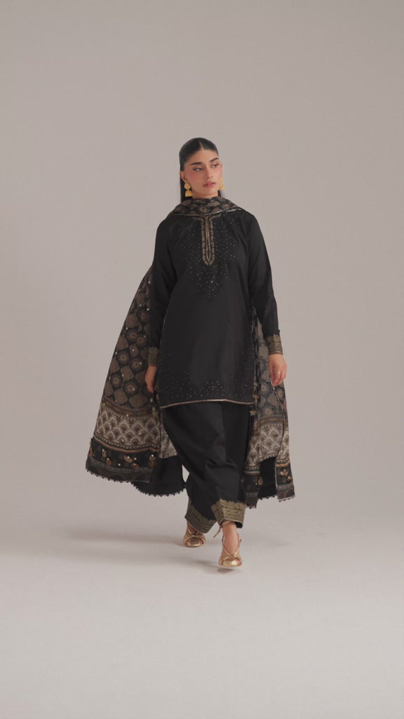 The Eclipse Set by Mannam is a black Pima cotton short kameez featuring monotone tilla embroidery, goti lace, tilla tassels and a cutwork back neckline in organza, paired with a balloon shalwar and an ajrak-inspired silk dupatta with sheesha work.